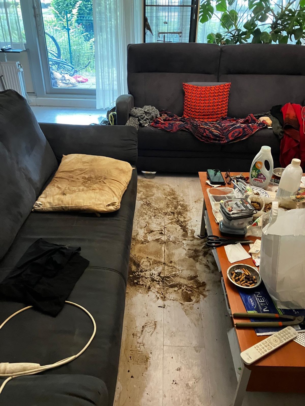 Woonkamer voor de ontruiming en schoonmaak, vol spullen en met een vervuilde vloer